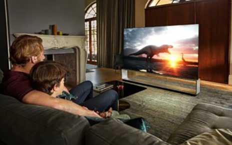 Father and son sit together in their living room to watch dinosaurs come to life on their LG TV.