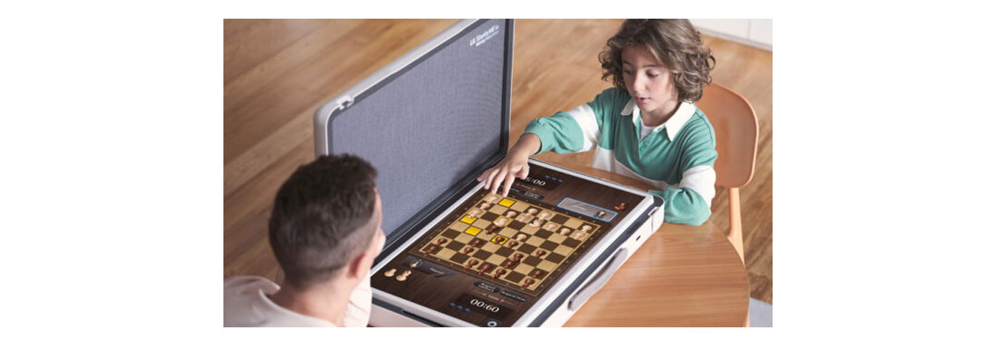 A father and son play a game of chess game at a desk using the LG StanbyME Go model in table mode.