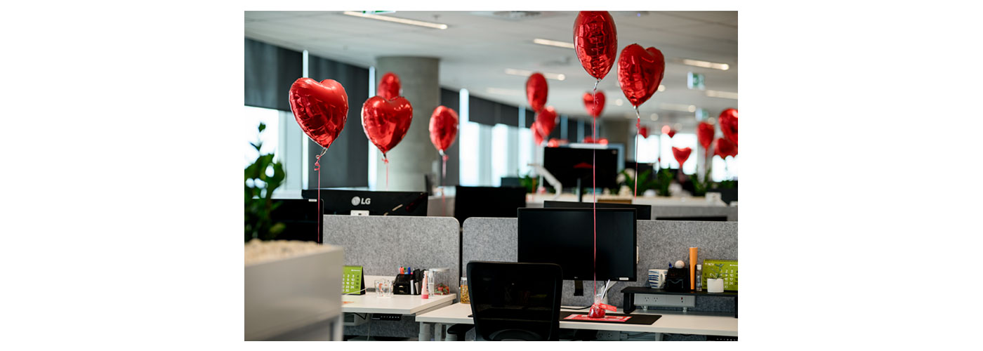 A photo of red heart balloons attached to workers' desks 