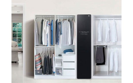 The LG Styler is placed in a room between two white open wardrobes full of clothes