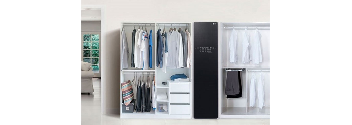 The LG Styler is placed in a room between two white open wardrobes full of clothes