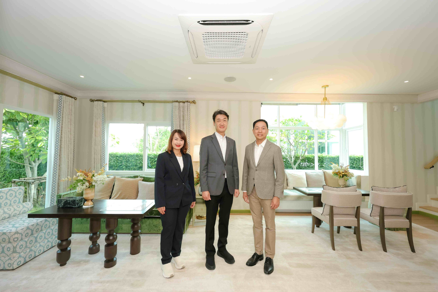 Three people stand in a modern living space below an air conditioner unit installed on the ceiling.