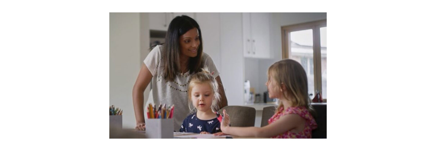 A female talking to kids who are drawing at the dining table
