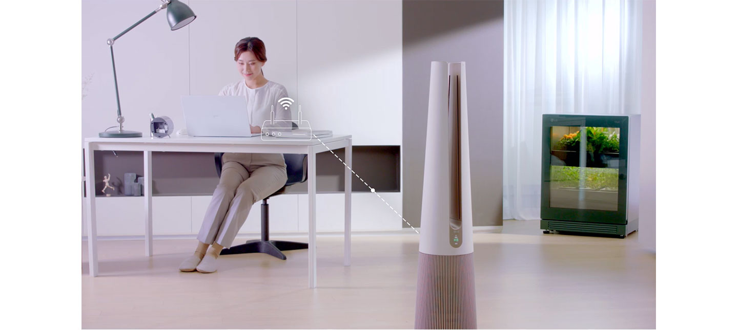 LG PuriCare AeroTower and LG tiiun installed in a space where a woman is working with a laptop on a desk
