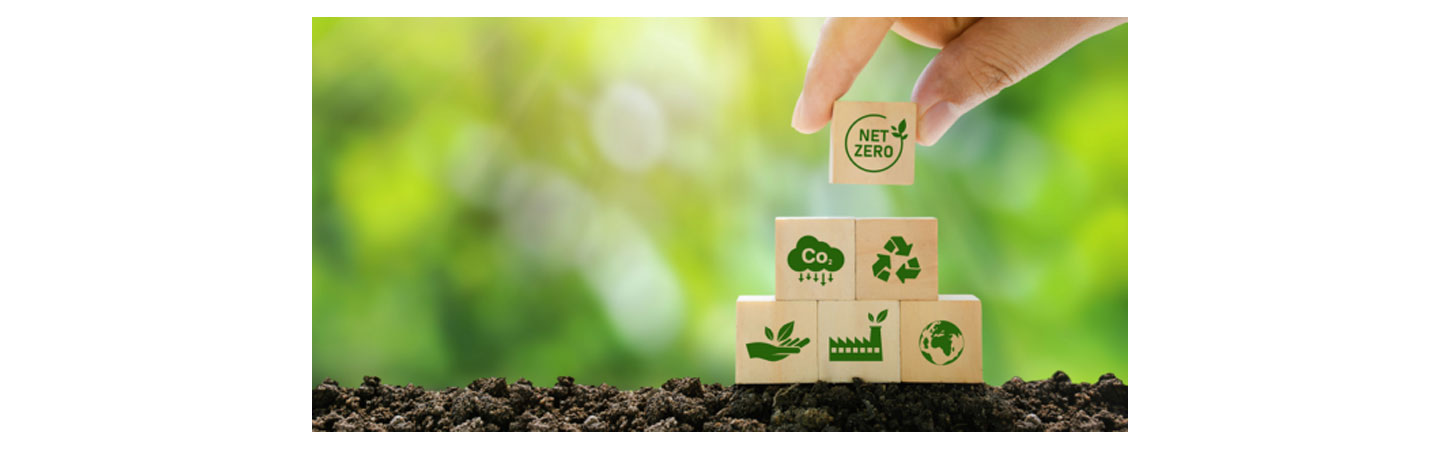 A human hand placing a wooden block that reads 'NET ZERO' on the top of bunch of blocks