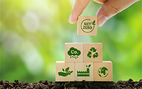 A human hand placing a wooden block that reads 'NET ZERO' on the top of bunch of blocks