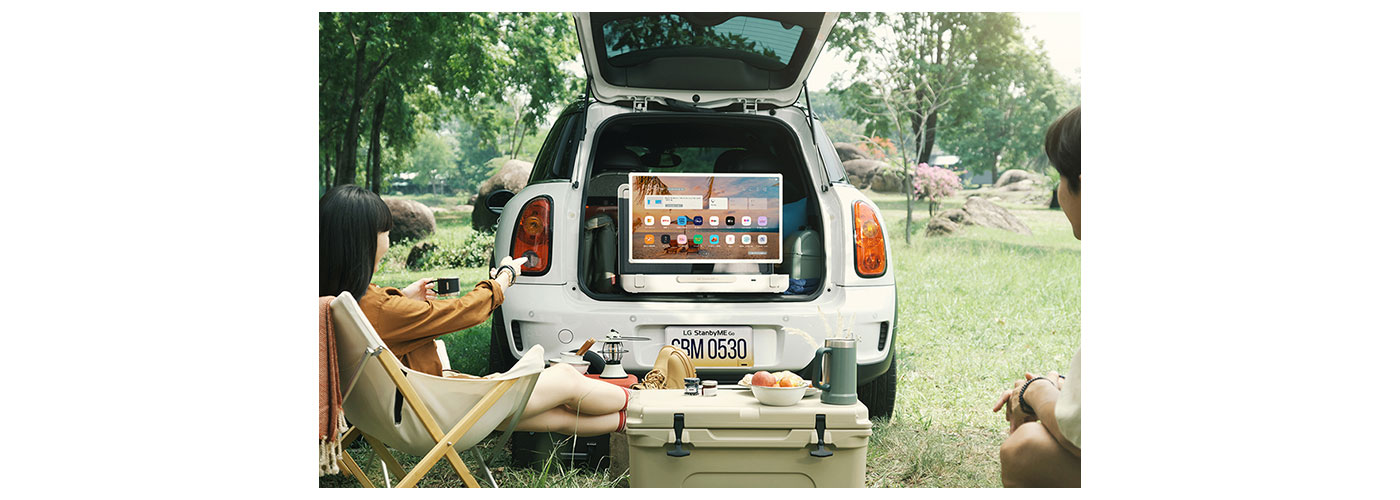 A photo a car trunk open with two people watching the LG StandbyME GO screen 