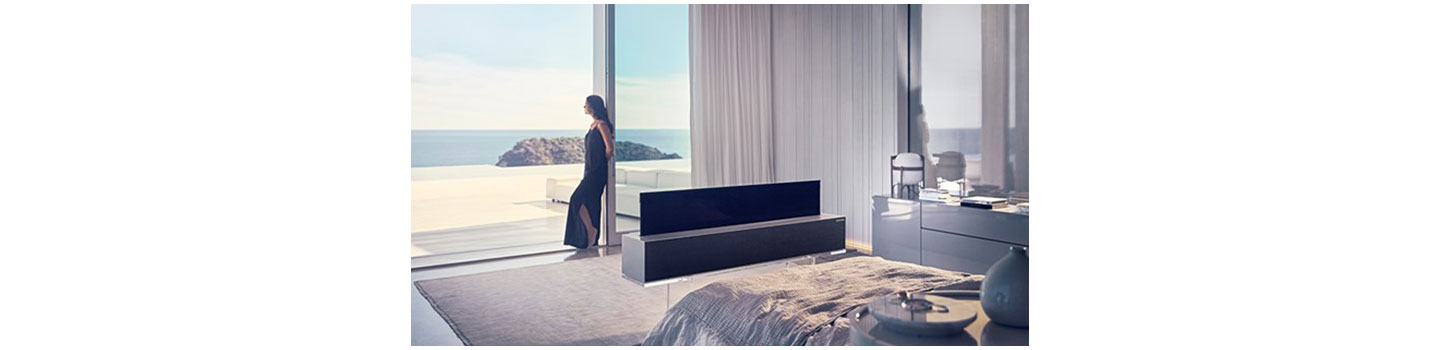 LG SIGNATURE OLED R installed in a luxury room where a woman is leaning against a big window