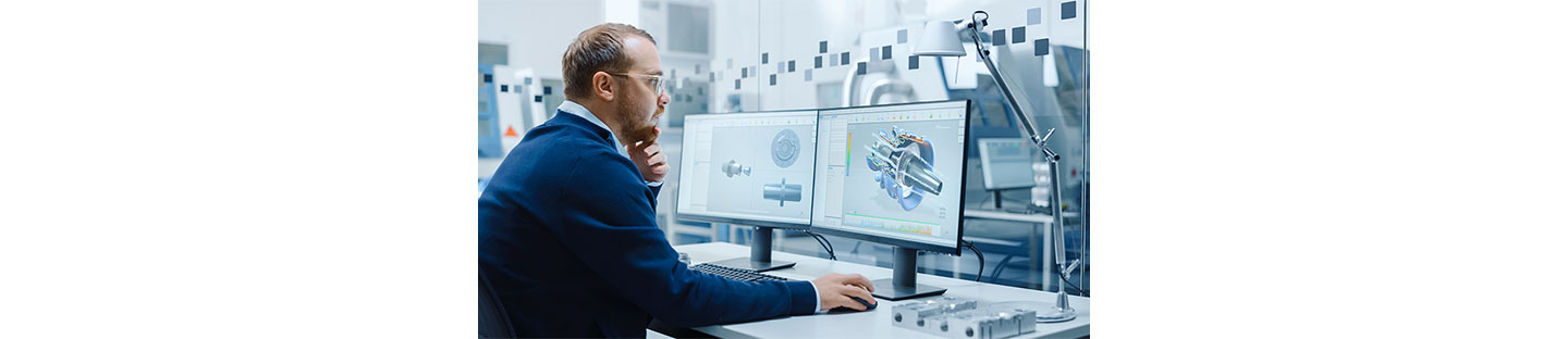 A photo of an engineer looking at an intricate system on a dual monitor