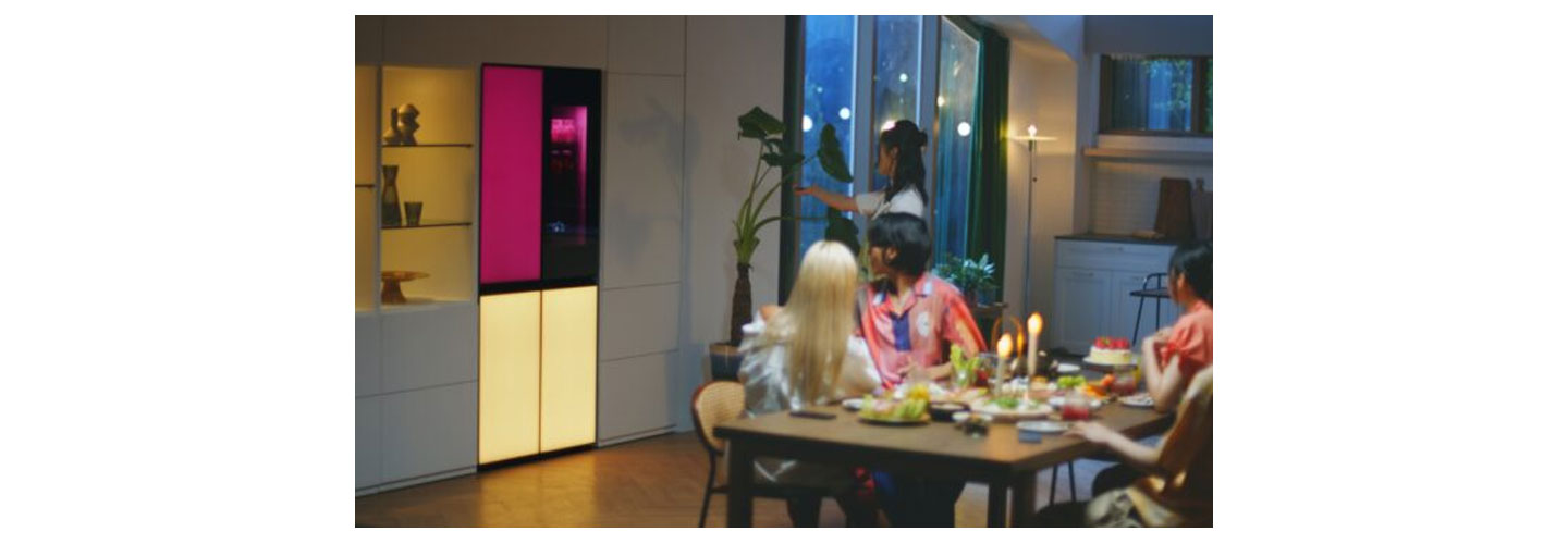 A woman is remotely playing music via a built-in Bluetooth speaker of the LG MoodUP refrigerator at a house party.