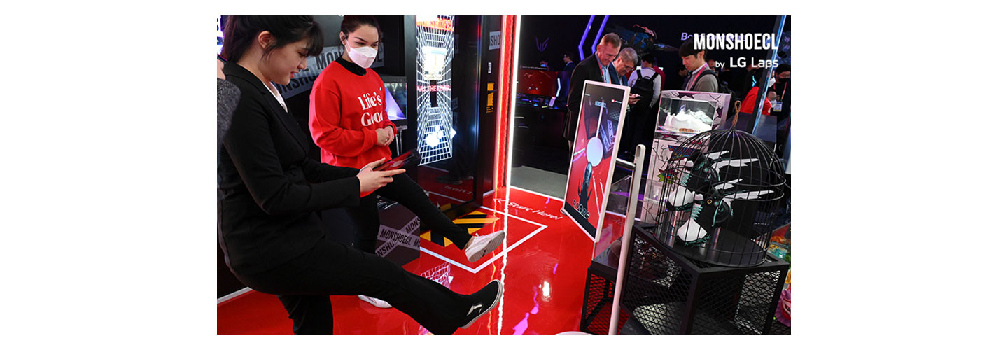 A corner of LG's booth decorated with Monshoecl products during CES 2023 where a visitor is trying on the shoe virtually with her smartphone