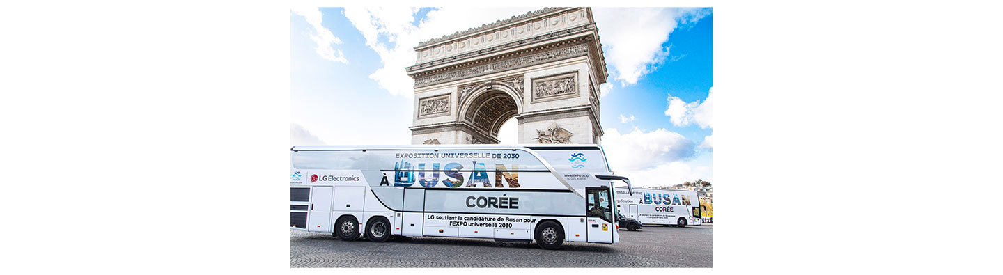 A photo of a big LG bus with the words 'A Busan Coree' passing by Arc de Triomphe