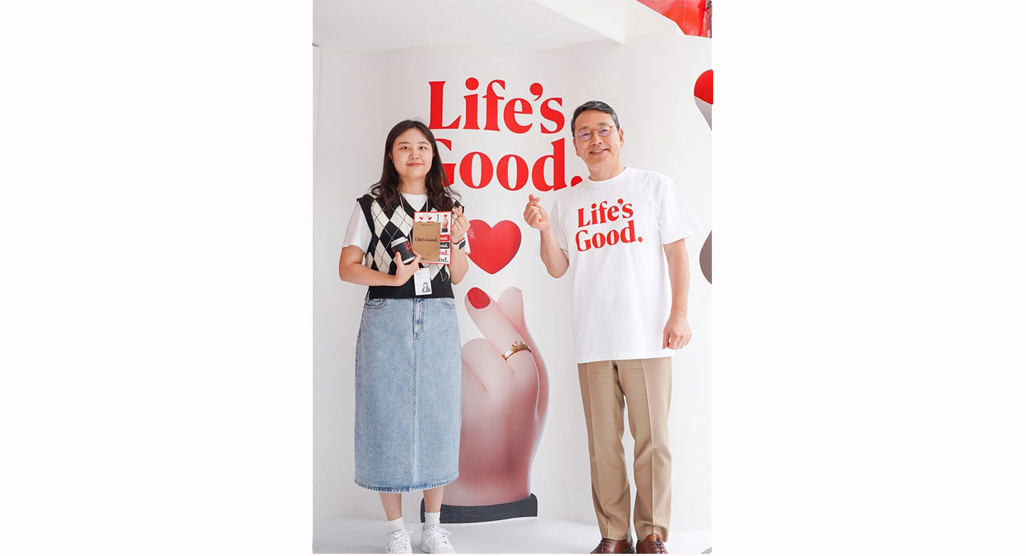 LG CEO posing with LG employee in front of the white wall decorated with a phrase 