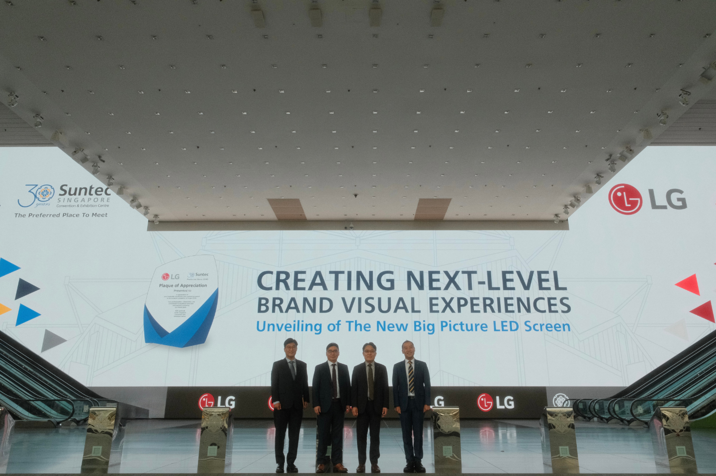 Four LG Electronics representatives are standing on a stage during the unveiling ceremony of the new Big Picture LED Screen, with a presentation titled "Creating Next-Level Brand Visual Experiences" in the background.