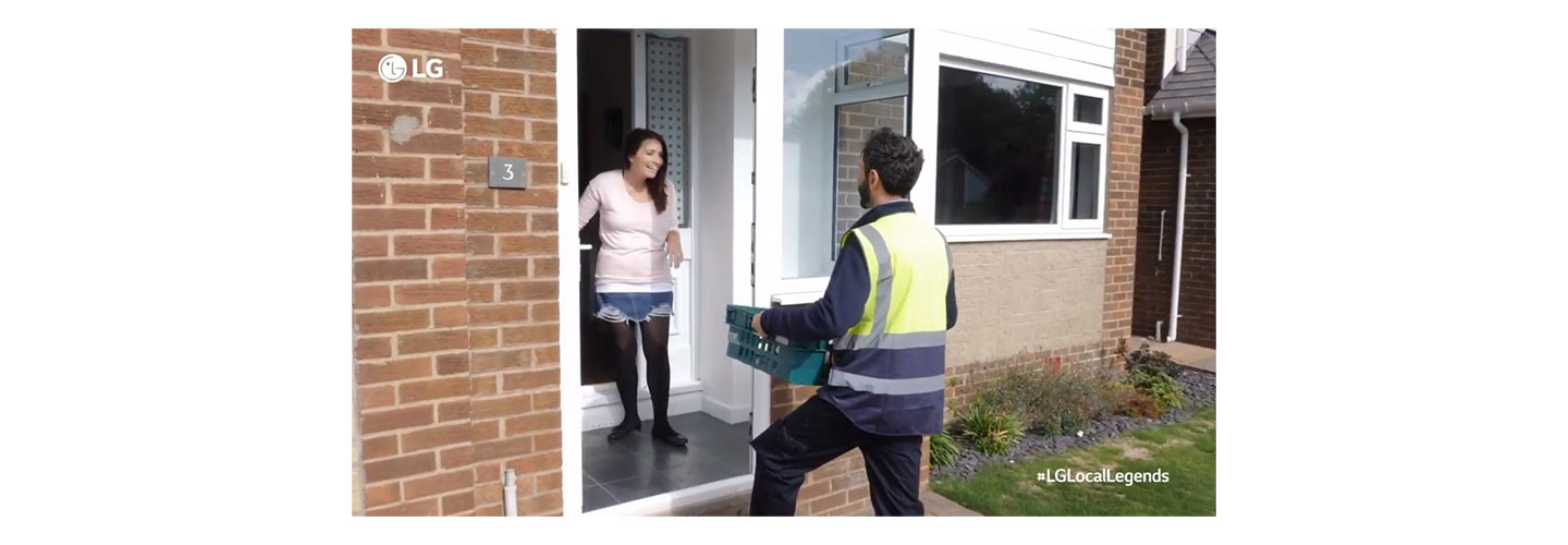 A woman looks overjoyed as a man pays a visit to her front door to gift a large box of groceries
