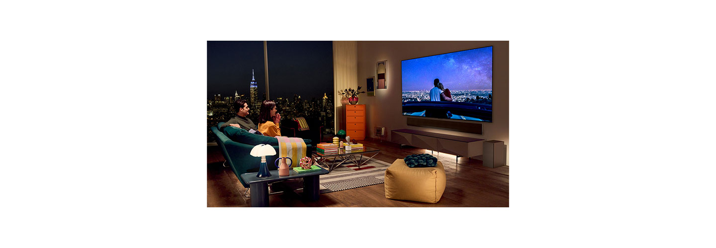 A couple watching a romantic movie on their LG OLED TV in a modern living room overlooking the New York City skyline at night