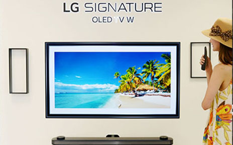 A woman looks at LG SIGNATURE OLED TV W which displays the tropical beach and coconut trees on its screen.