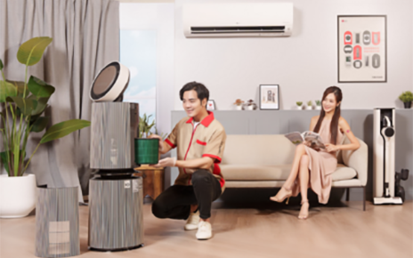 A photo of a woman sitting on a couch in a showroom with LG products and a man next to an LG PuriCare