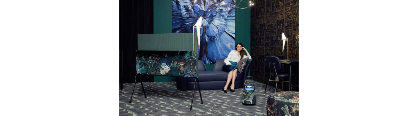A woman watches LG OLED Objet Collection Posé next to LG XBOOM 360 portable speaker, which both sport an artistic design by Dutch brand Moooi, as she sits in a room full of artwork
