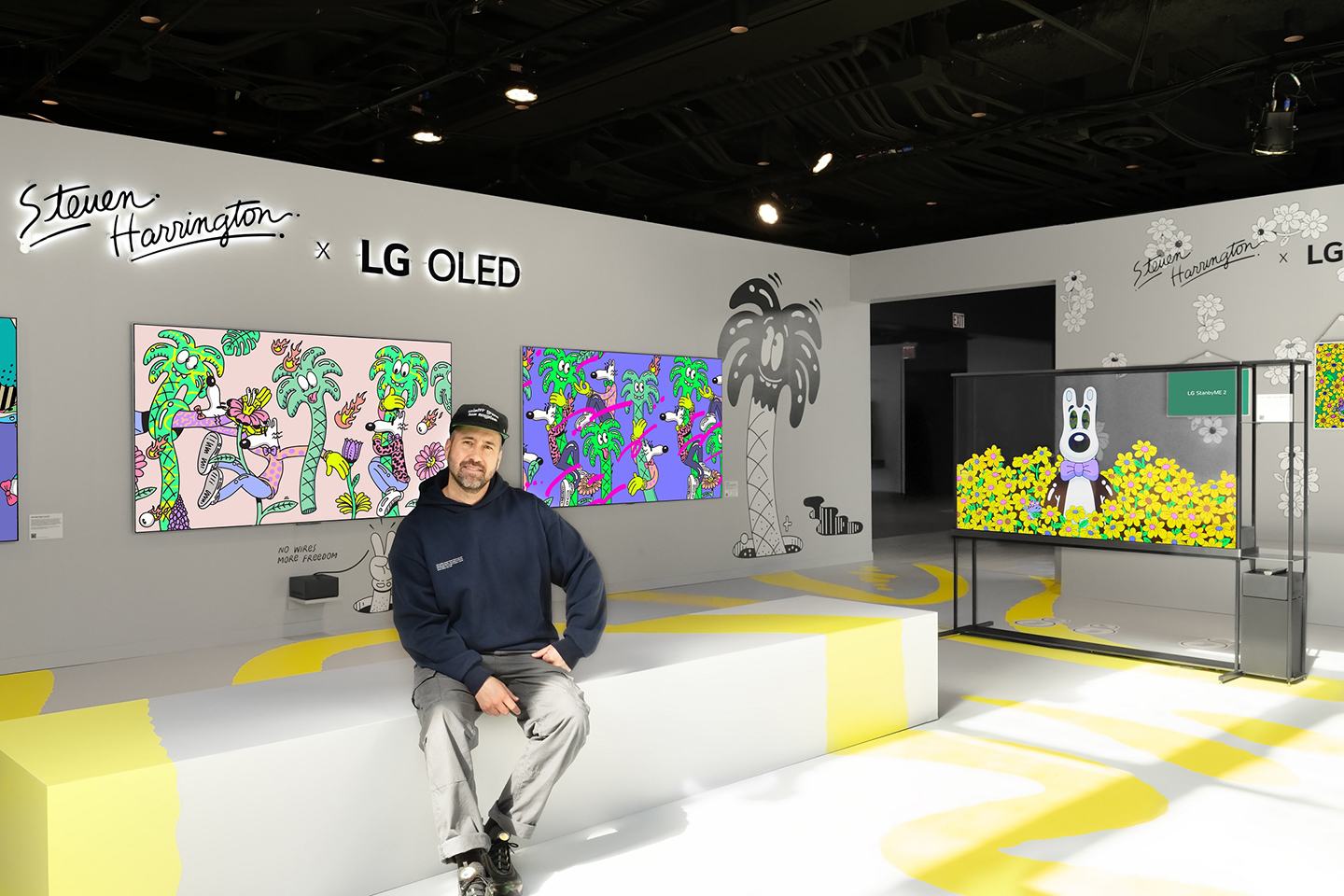 A photo of a man sitting on a couch in front of artworks in an exhibition
