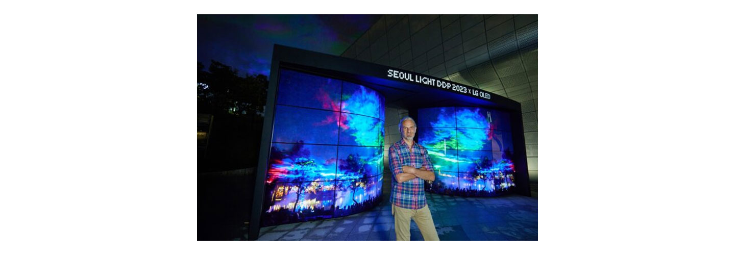 Artist Dan Archer standing in front of the Seoul Light DDP 2023 with numerous panels displaying his vibrant artwork