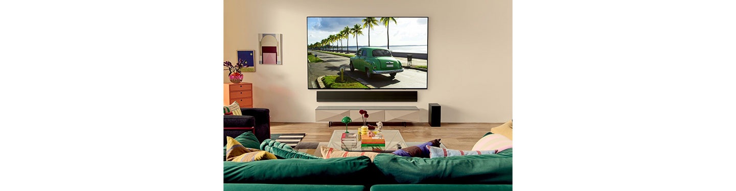 LG OLED TV in a bright living room displaying a green car driving down a road by the beach
