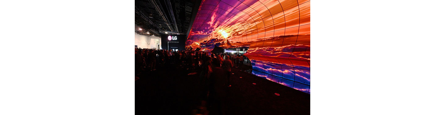 A crowd enter the LG OLED TV showroom at CES through an expansive installation of LG displays depicting a beautiful sunrise