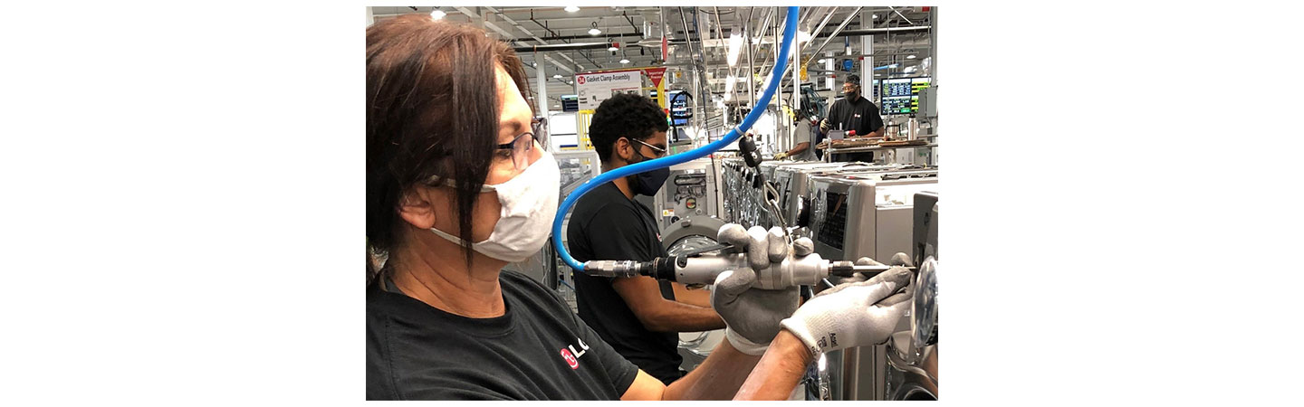One LG factory worker using special equipment to assemble the washing machine’s front panel while others work in the background
