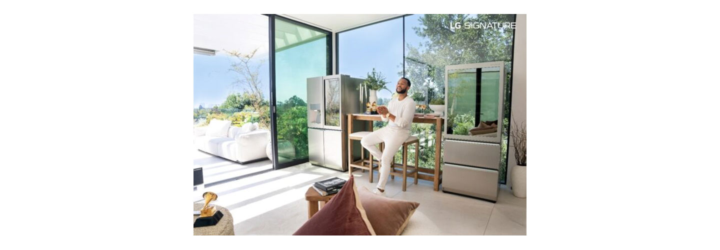 John Legend sitting on a stool between the LG SIGNATURE InstaView Door-in-Door refrigerator and LG SIGNATURE Wine Cellar