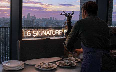 A chef preparing food as he looks out on to the London skyline and “LG SIGNATURE” neon sign