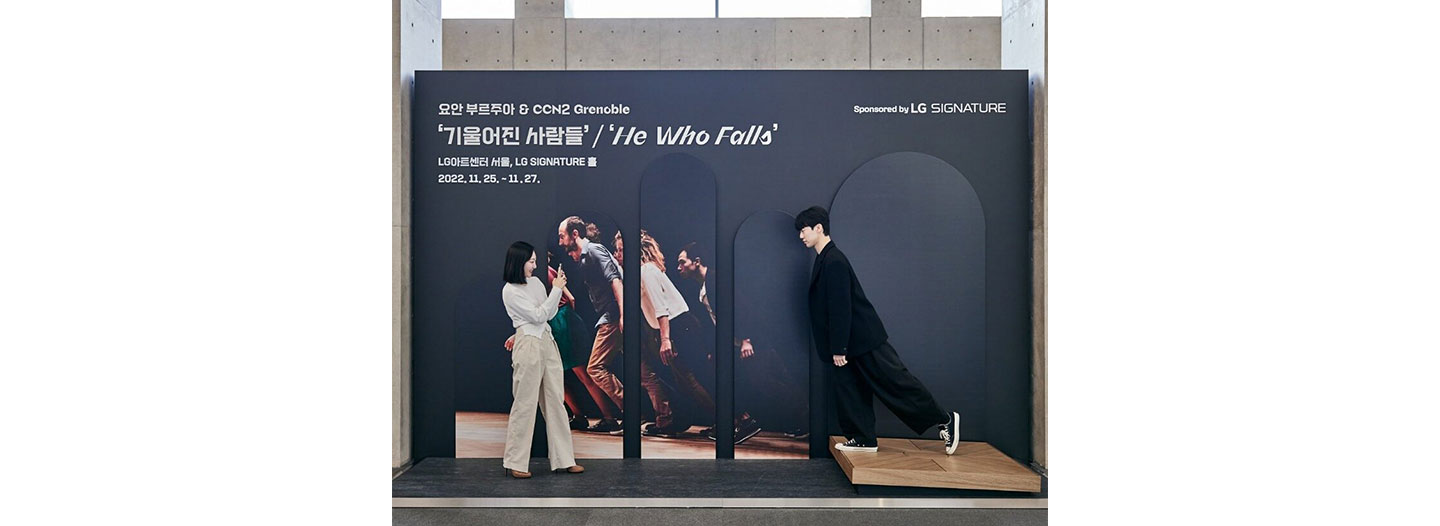 A man posing in front of the He Who Falls photo zone in the LG SIGNATURE Hall as a woman takes a photo