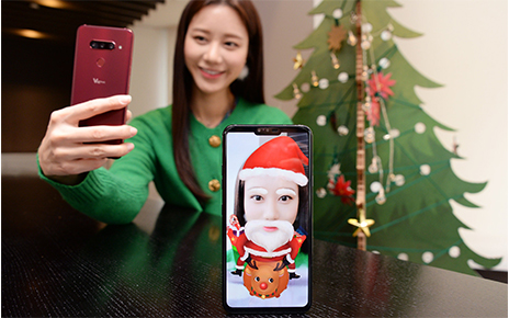 A woman turns her selfie into a Santa Claus lookalike by using the Augmented Reality (AR) sticker function of LG V40 ThinQ.