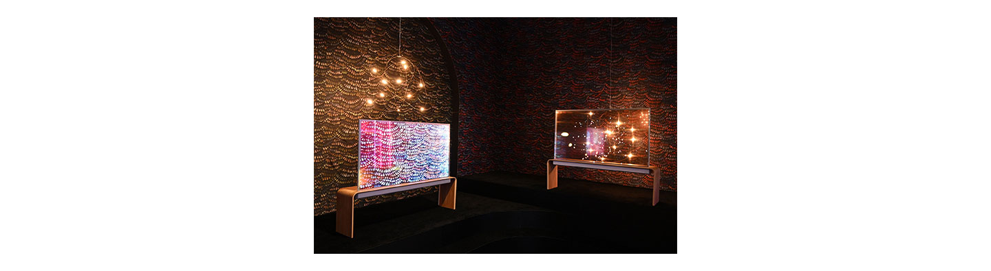 Two of LG’s newly unveiled LG Transparent OLED model displayed in a dark room with bright lights, one transparent and the other displaying content.