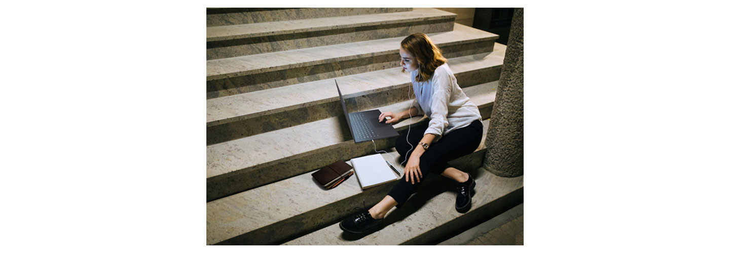  A woman casually sitting down on the stairs while working with her LG gram and a notebook.