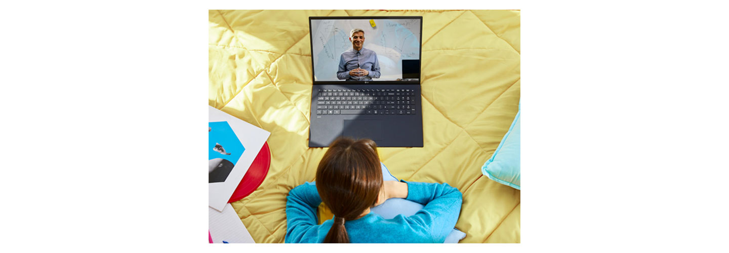 A woman relaxes on her bed while using her LG gram to take a lesson from a teacher online.