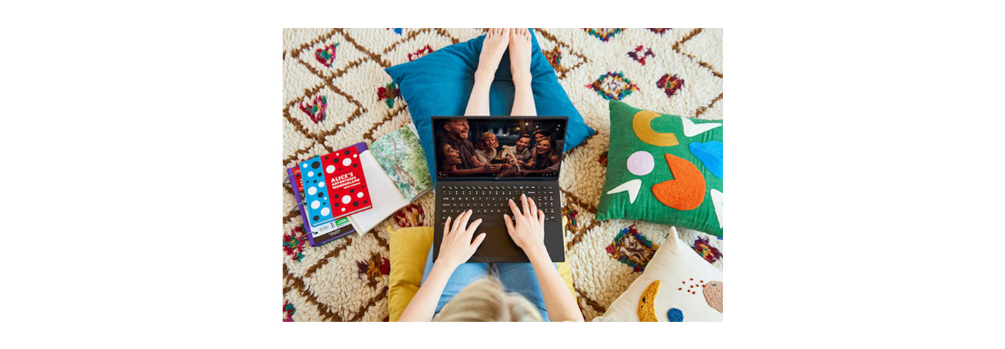 A woman sitting comfortably on the floor with colorful cushions as she watches a TV show on her LG gram.