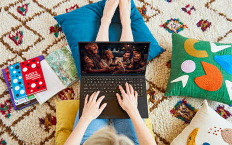 A woman sitting comfortably on the floor with colorful cushions as she watches a TV show on her LG gram.