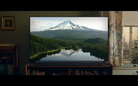 LG's TV displays a beautiful mountain, forest and lake inside a living room.