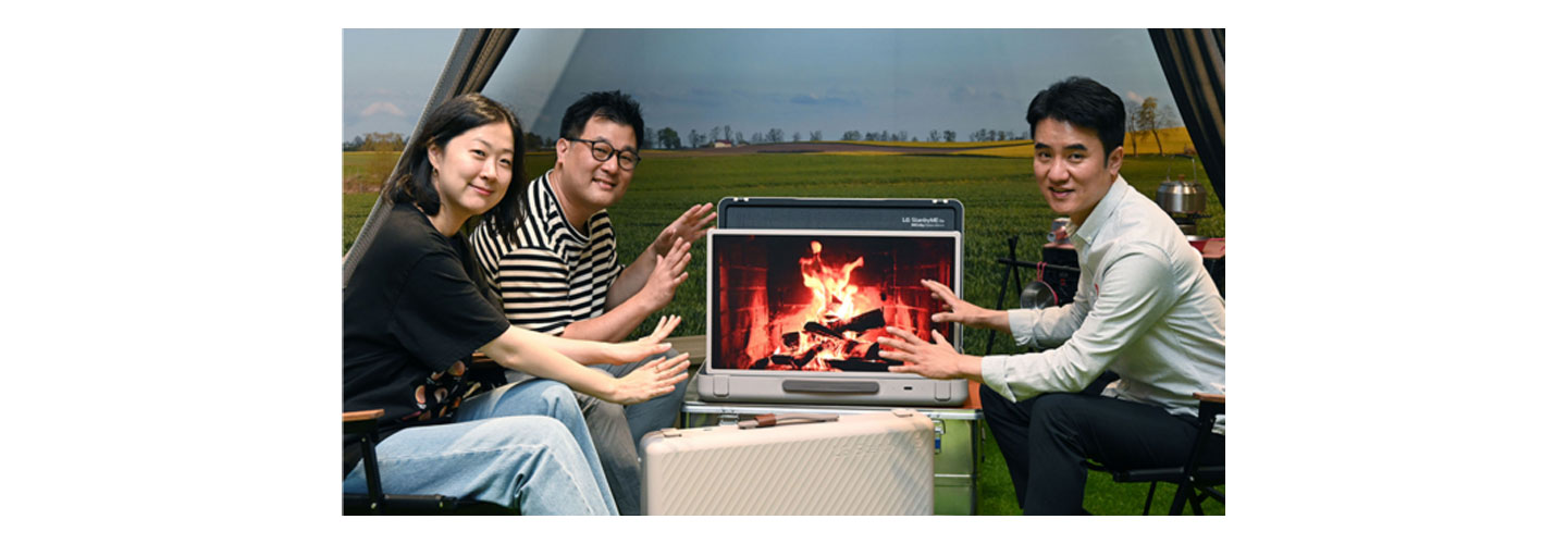 Three LG representatives sitting around a display of a campfire on the LG StanbyME Go model