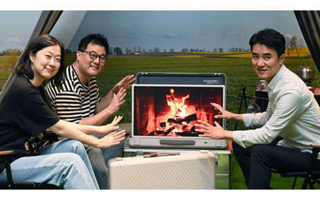Three LG representatives sitting around a display of a campfire on the LG StanbyME Go model