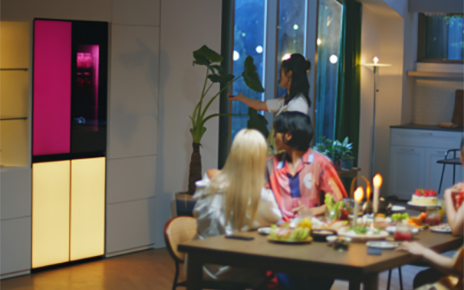 A woman is remotely playing music via a built-in Bluetooth speaker of the LG MoodUPTM refrigerator at the house party