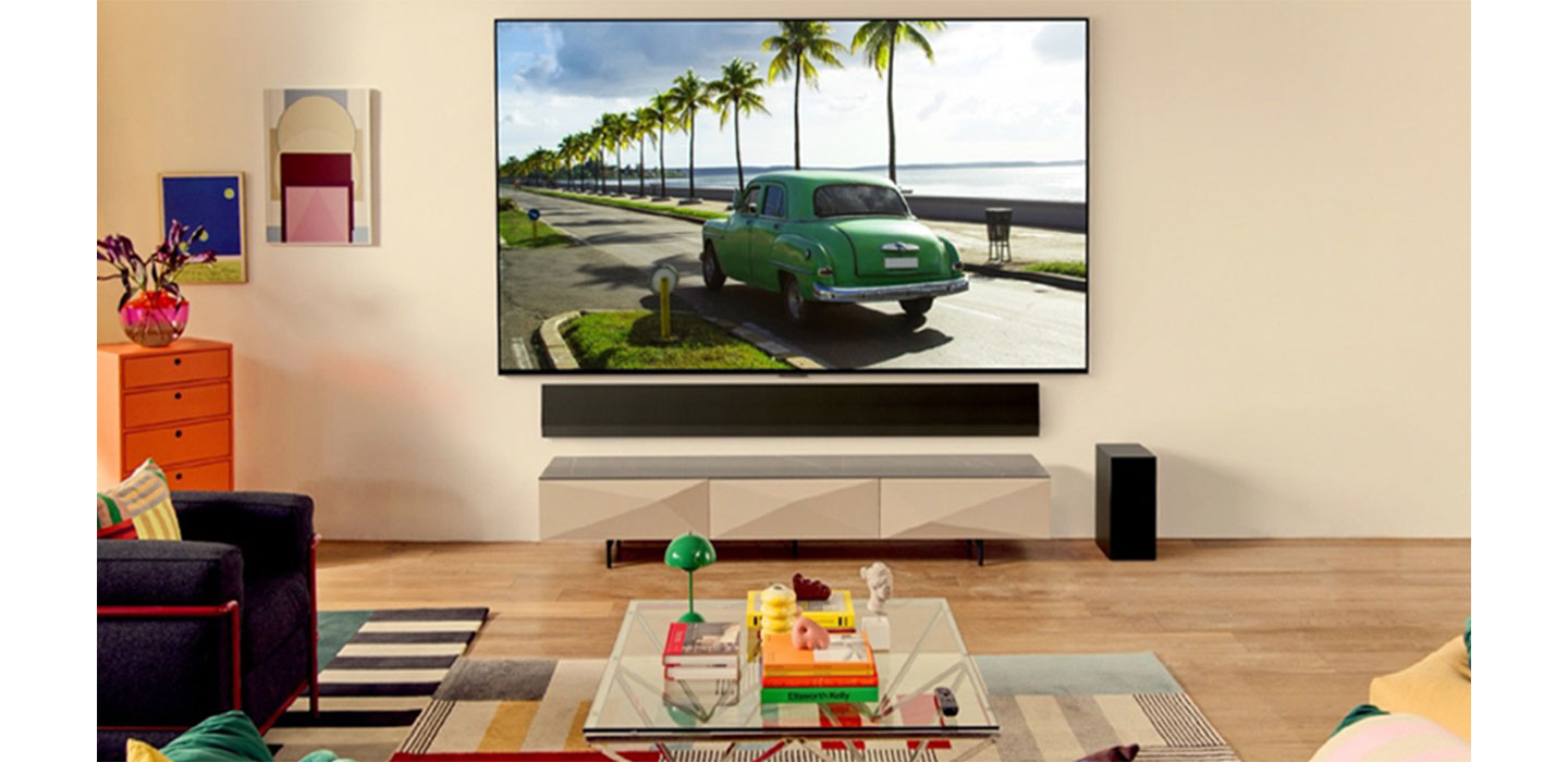 LG OLED TV in a bright living room displaying a green car driving down a road by the beach