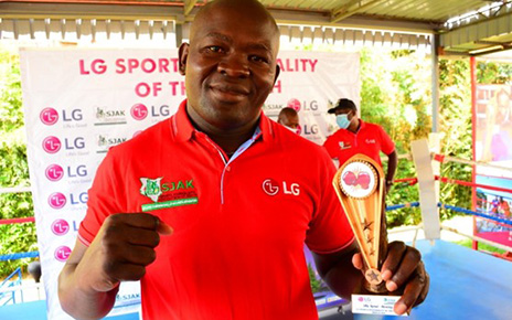 A photo of boxer Elly Ajowi making a proud fighting pose while holding his LG trophy