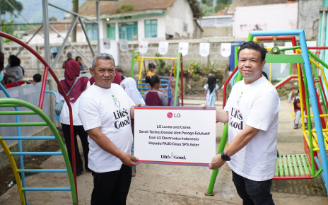 Two men are holding a sign that reads "LG Loves and Cares," with children playing on a playground in the background.