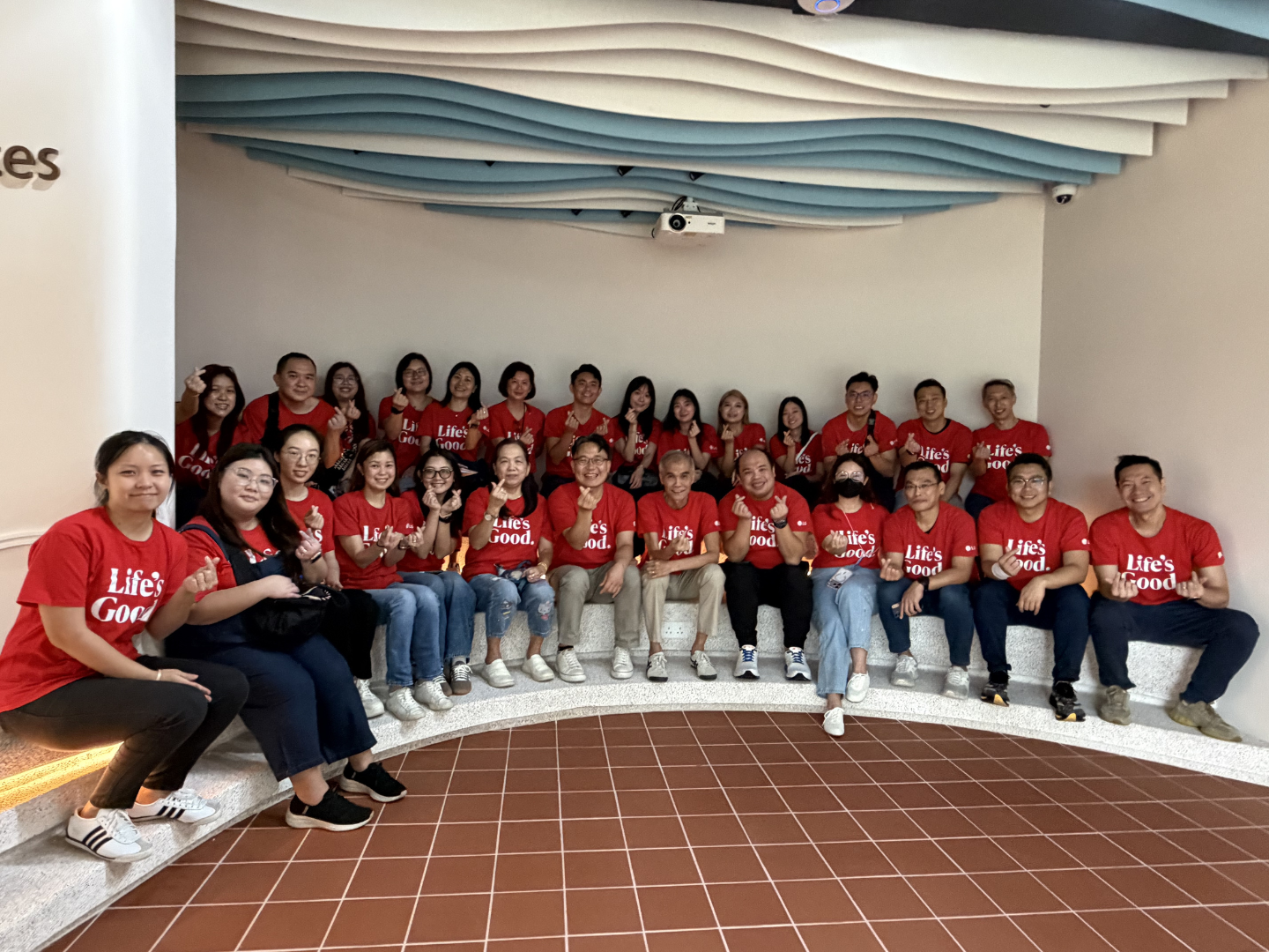 Volunteers wearing red "Life's Good" t-shirts pose by making a small heart shape with their hands.