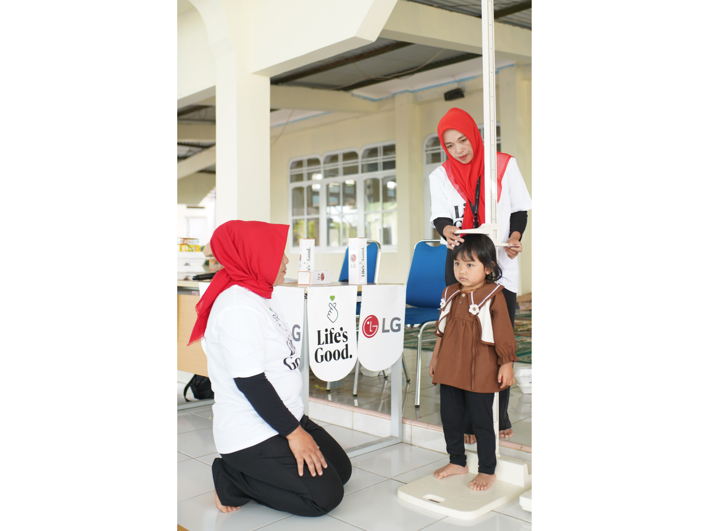 A girl measures her height next to a desk with the "Life's Good" logo. 