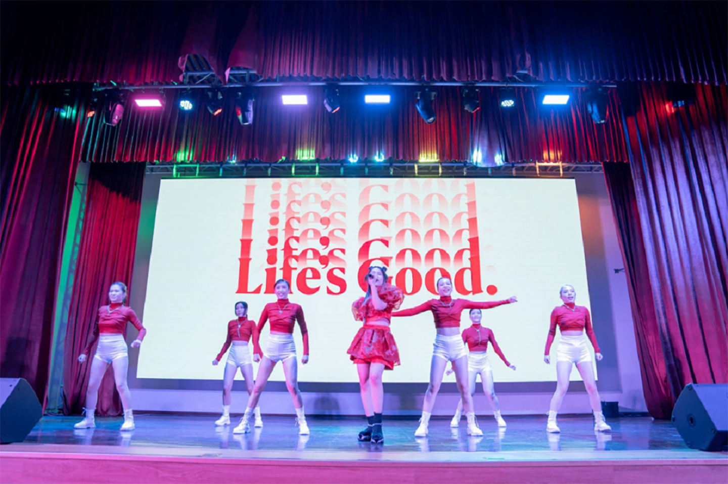 A picture of people performing on stage with the Life's Good logo behind