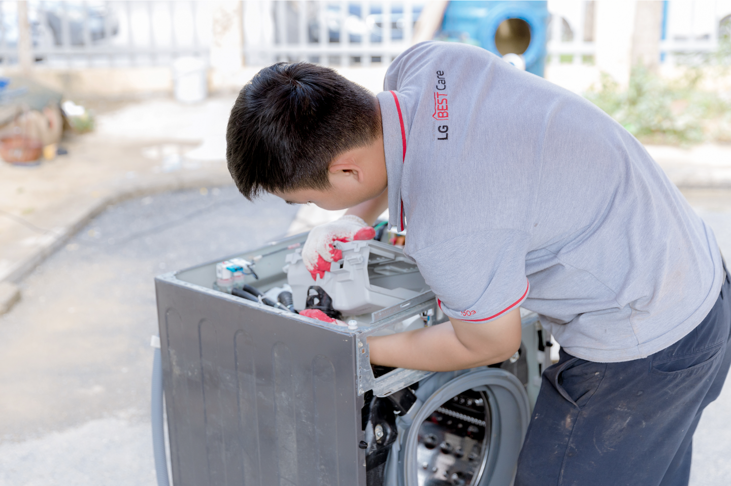An LG employee wearing an LG BEST Care uniform repairs a washer on the road.