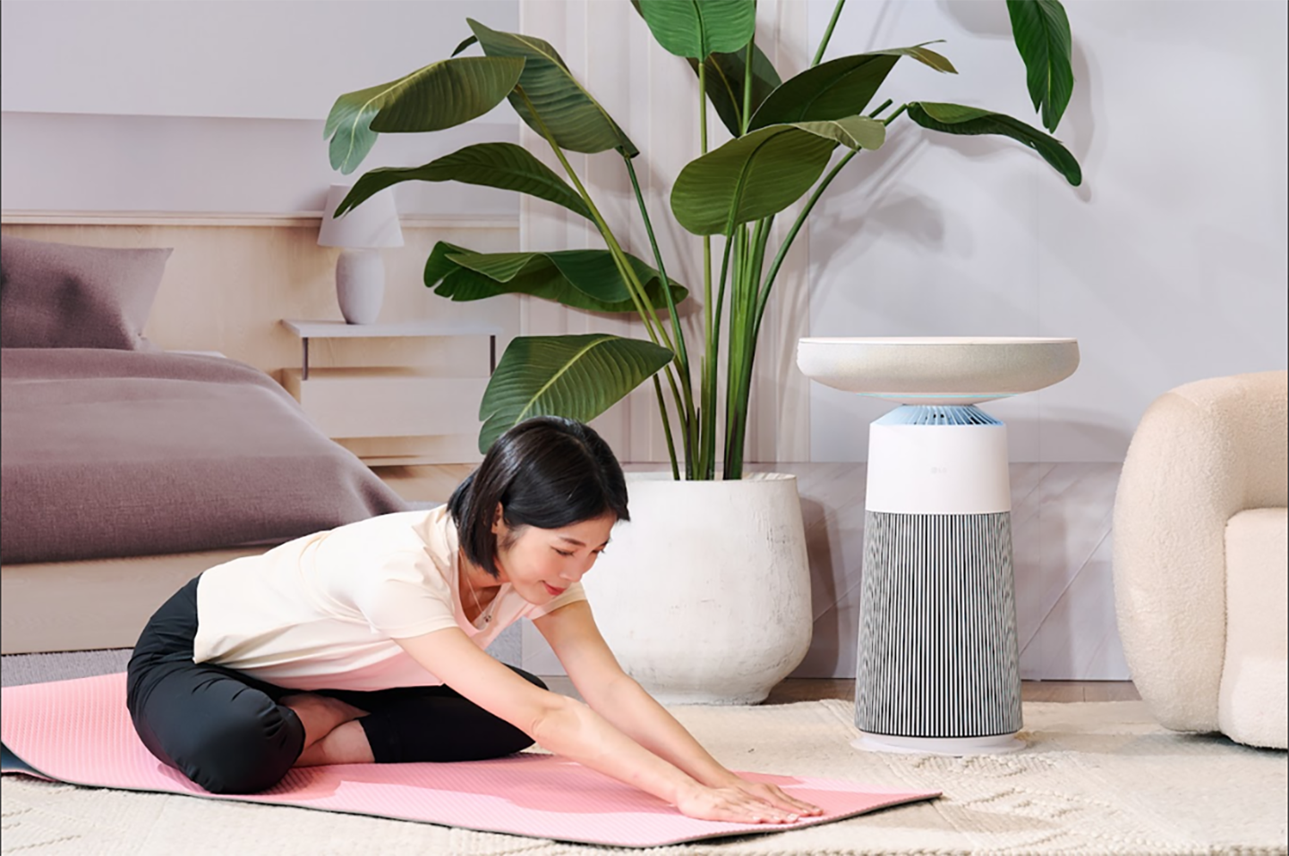 A woman is stretching on a pink yoga mat beside the LG PuriCare AeroSpeaker in the AI Living Zone, with a large indoor plant in the background.