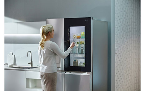 A woman knocking on her LG Door-in-Door refrigerator’s window to look inside without opening the door